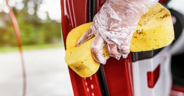 年轻女子在清洗车门的一部分，特写细节是戴着手套的手拿着黄色海绵图片下载