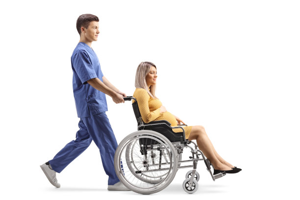 男医护人员用轮椅推着孕妇的全身照图片下载