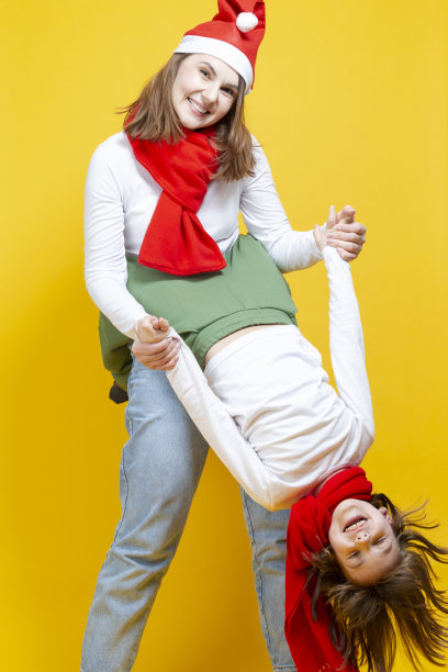 两个美丽的白人女士的肖像不同的年龄在圣诞帽和休闲衣服一起玩在时髦的黄色背景。图片下载