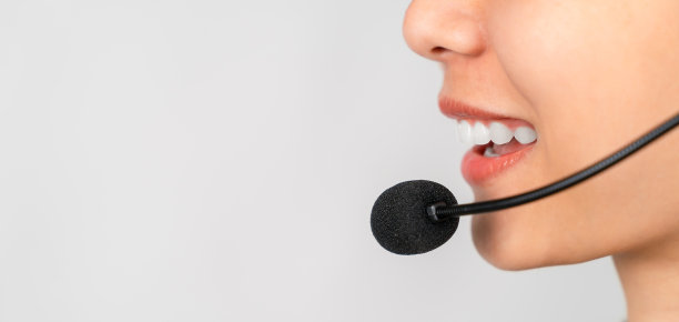 近脸微笑的女人戴着耳机是客户支持电话接线员，咨询服务呼叫中心在灰色的背景上。图片下载