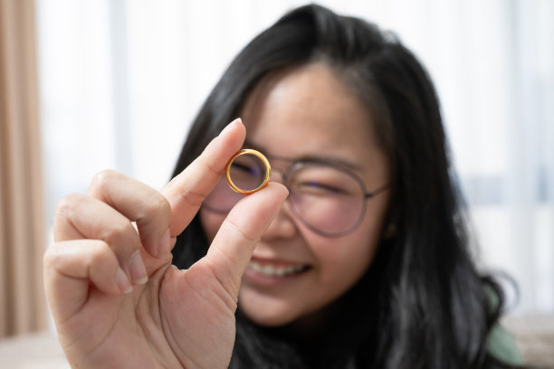 靠近美丽的眼镜亚洲女人正在她的卧室里玩金戒指图片下载