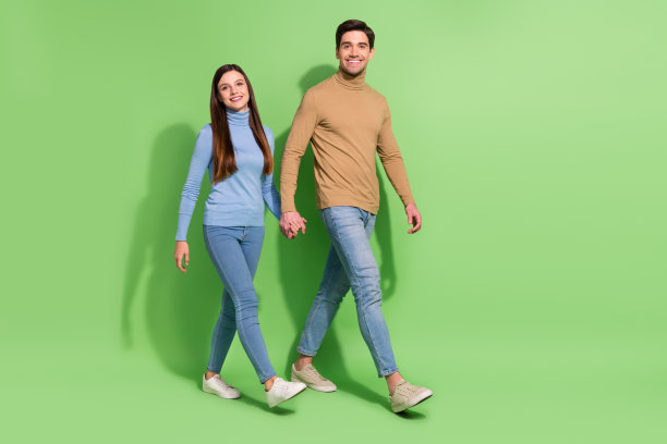 照片上一对对喜气洋洋的情侣牵着手散步，周末旅行，穿着休闲装，孤立的绿色背景图片下载