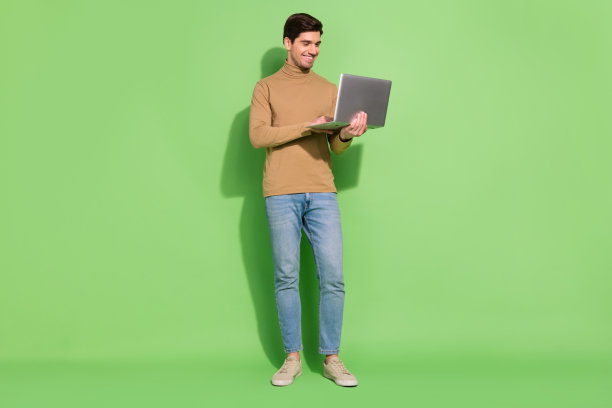 照片开朗的自由职业者程序员家伙打字电子邮件信息穿米色衬衫牛仔裤孤立的绿色背景图片下载