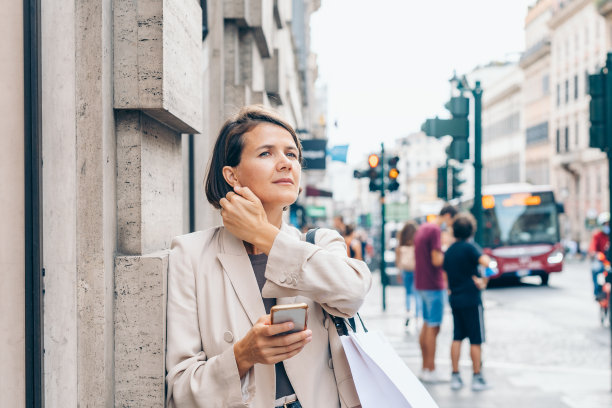 年轻时尚的女子在城市的街道上，手里拿着一部智能手机，手里拿着一个大包裹图片下载