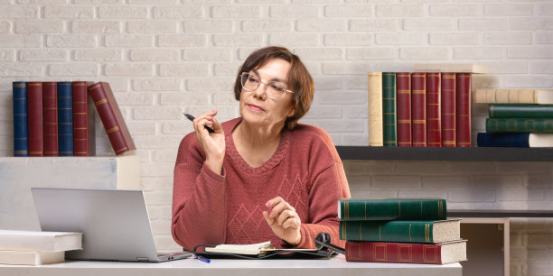 一位年长的女性在办公室里对着笔记本电脑显示器工作。格式照片2 x1图片下载