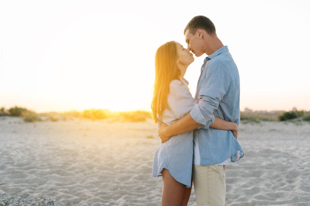 浪漫的情侣在海滩上穿着休闲的衣服在日落时接吻。在热带度假胜地度蜜月的概念。横幅。图片下载