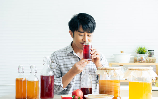 肖像俊男面带清新幸福的微笑，手拿康普茶健康益生菌发酵茶饮料红苹果，草莓，蘑菇scoby在家中厨房。图片下载