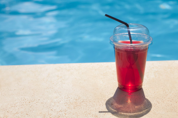 清爽多汁的饮料在一个外卖塑料杯旁的游泳池在一个炎热的一天在度假酒店图片下载