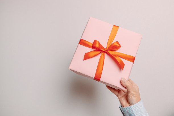 商务女性手握纸礼品盒与红色缎带装饰在灰色的背景图片下载
