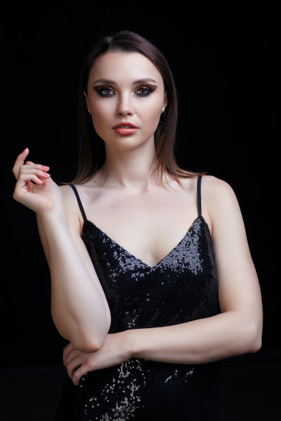 漂亮的年轻女子穿着黑色的连衣裙，脸上带着闪亮的妆容。图片下载