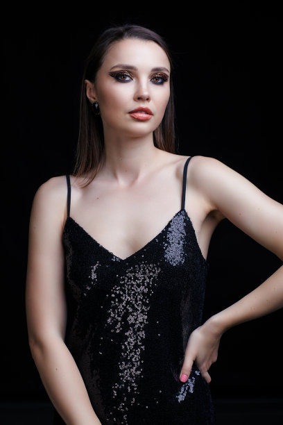 漂亮的年轻女子穿着黑色的连衣裙，脸上带着闪亮的妆容。图片下载