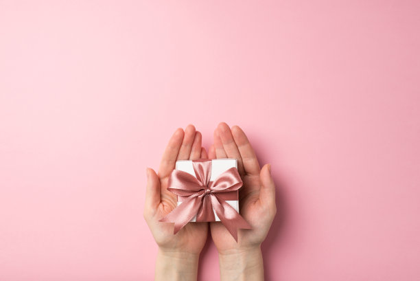 第一人称俯视图照片的情人节装饰女性手拿白色小礼盒与粉红色丝带蝴蝶结在手掌上孤立的粉彩粉红色背景与空白空间图片下载
