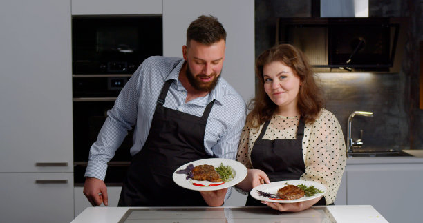 一对美食博主夫妇拿着烤牛排的盘子，对着镜头做手势图片下载