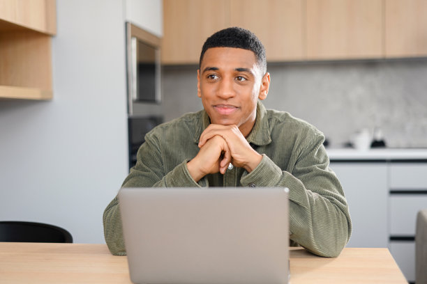 一名开朗的多种族男性员工坐在办公室里休息，坐在笔记本电脑前，把目光移开图片下载