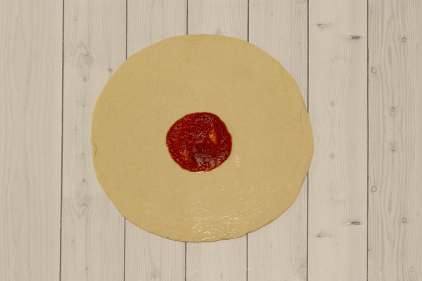 把番茄酱撒在木桌上的披萨面团上。图片下载
