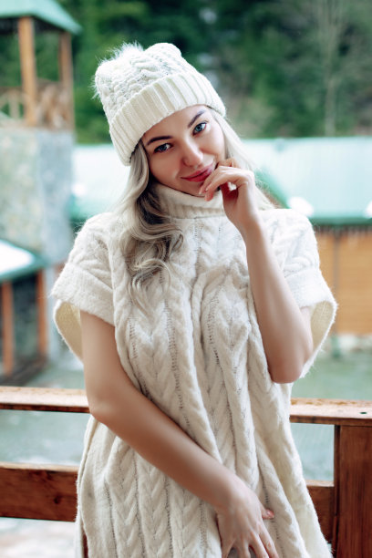 一个漂亮的女孩戴着白色的帽子和毛衣在阳台上的街道上的肖像。温暖的冬天的衣服图片下载