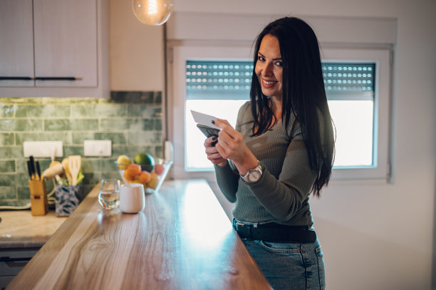 中年妇女拿着信用卡，在家里用智能手机图片下载