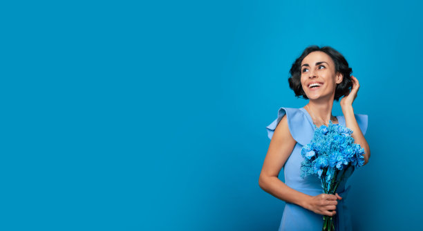 这张照片上，一位穿着优雅蓝色连衣裙的美丽年轻女子正拿着一束新鲜的蓝色鲜花摆姿势。母亲的一天。女人的假期。春天。女性的权利图片下载