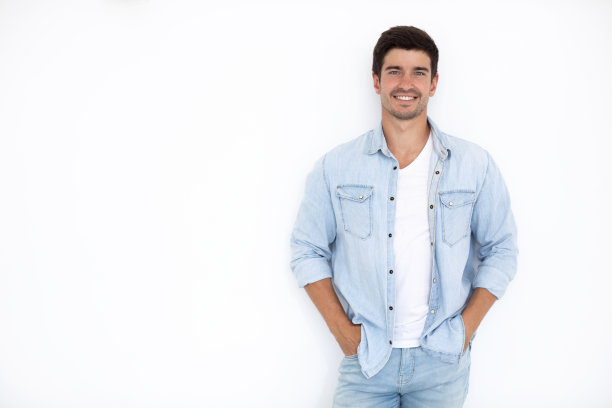 年轻英俊的男子面带笑容，露出牙齿，身穿白色背景的牛仔衬衫。图片下载