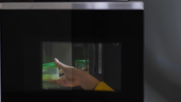 在家里，妇女用现代微波炉加热一盒食物作为零食午餐图片下载