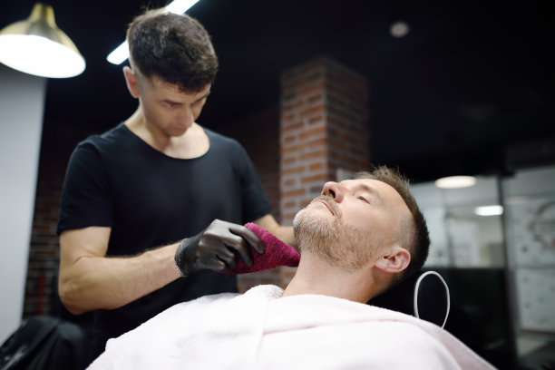 理发师大师在沙龙用直剃须刀剃英俊成熟的大胡子男人。发型艺术家为男士理发店的人制作胡须造型。专业造型师服务。图片下载