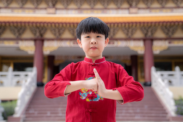 英俊的亚洲男孩穿着中国传统的红色服装站在寺庙与模糊的背景。在中国农历新年庆祝快乐的微笑。对你表示尊重。素材图片