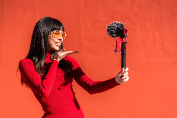 漂亮的黑发女孩亲吻，用手机和麦克风录制视频博客，穿着社交网络的裙子。白种人漂亮一个红色的背景，复制空间和粘贴图片下载