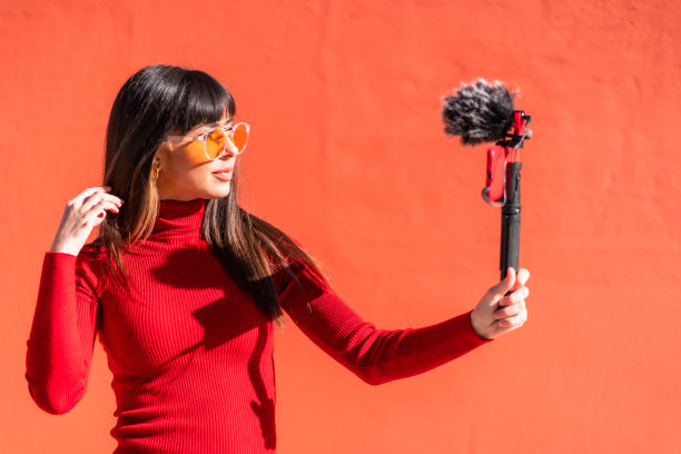 黑发女孩用手机和麦克风录制视频博客，穿着社交网络的裙子。白种人漂亮一个红色的背景，复制空间和粘贴图片下载