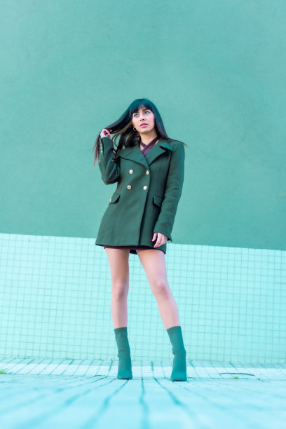 深色头发的模特穿着夹克和绿色的靴子在街上微笑。白种人漂亮的绿色和蓝色背景，垂直照片图片下载