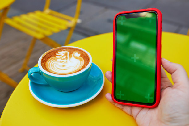 一杯新鲜的白咖啡，配上牛奶和绿色屏幕的智能手机图片下载