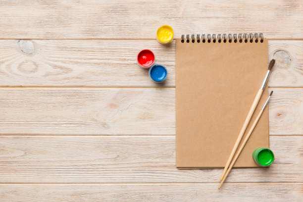 相册页和油漆，铅笔，画笔上的彩色背景。顶部视图与空的空间。工作场所的创造力。家庭教学概念图图片下载