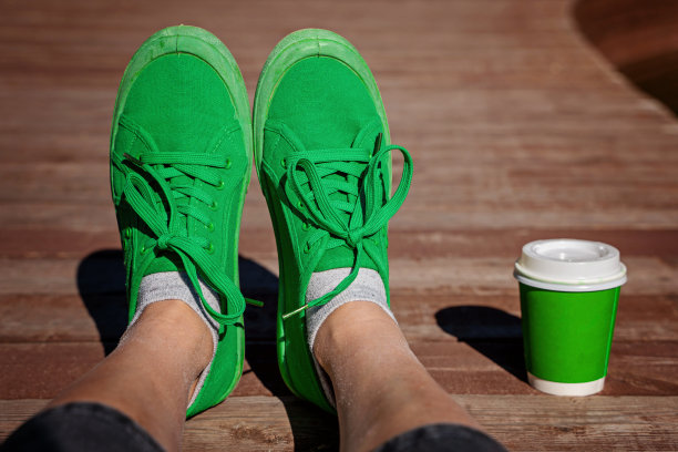 穿着绿色运动鞋的年轻女子用一次性杯子喝咖啡图片下载