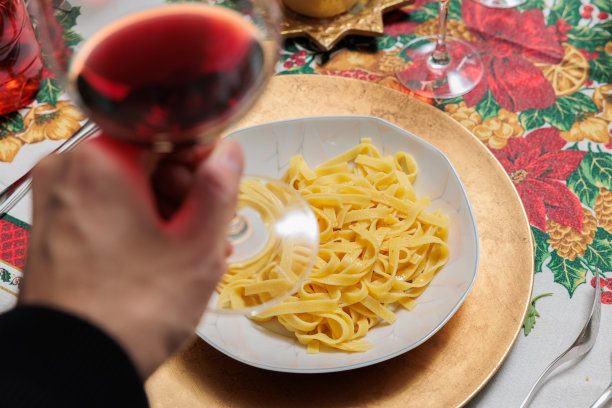 在圣诞节的时候，手端着红酒酒杯，手端着一盘配着酱汁的黄色意大利面图片下载