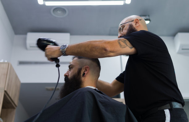 有纹身的男理发师正在给他的客户吹头发图片下载