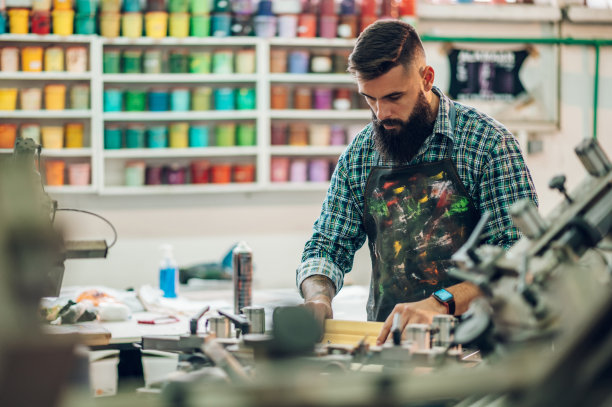 车间里，男性工人在使用印刷机时，将油墨压在画框上图片下载