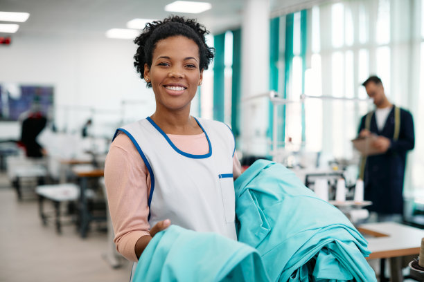 快乐的黑人女裁缝在纺织厂工作，看着相机。图片下载