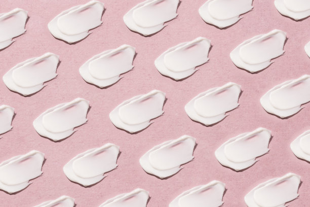在粉红色的背景上涂抹奶油。图片下载