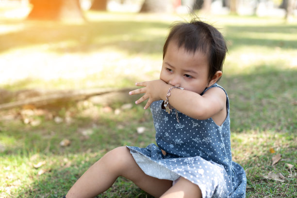 年轻的亚洲小孩坐在户外公园的草地上，沮丧和担心的痛苦，哭愤怒和害怕。悲伤的表情。图片下载