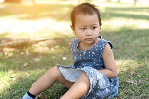 年轻的亚洲小孩坐在户外公园的草地上，沮丧和担心的痛苦，哭愤怒和害怕。悲伤的表情。图片下载