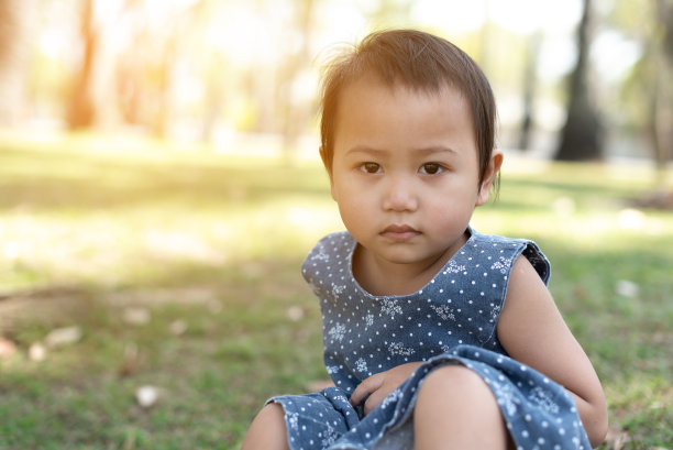年轻的亚洲小孩坐在户外公园的草地上，沮丧和担心的痛苦，哭愤怒和害怕。悲伤的表情。图片下载