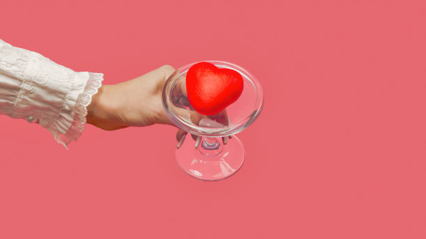 一个女人的手在玻璃盘子上盛着一颗红心。珊瑚背景上的美丽礼物。最小的情人节或周年纪念概念。创意爱情或情人节的概念。喜欢甜点。图片下载