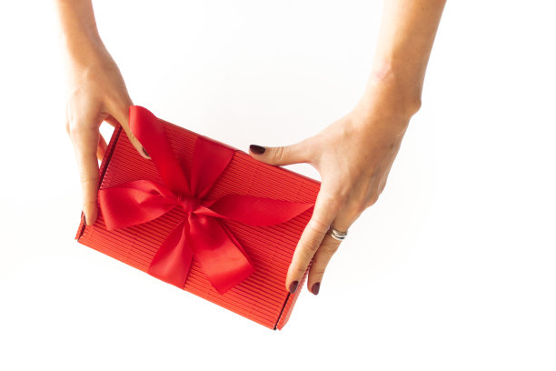 红色的礼盒上带着一个大大的红色丝带蝴蝶结在女孩手中，俯视图。女孩接受了一份礼物。这个女孩送了一份节日礼物。白色干净的背景文字和广告图片下载