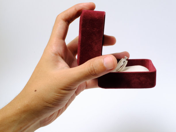 在白色背景的红色首饰盒里，手拿着订婚戒指图片下载