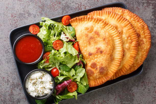 切布瑞基是一种克里米亚鞑靼人的美食，配上新鲜的沙拉和酱汁，放在盘子里。水平的俯视图图片下载