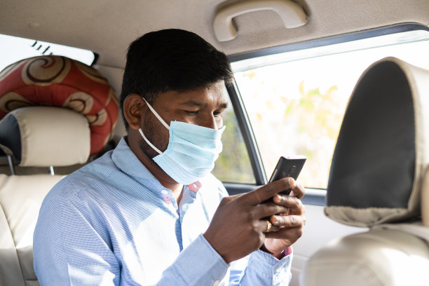带医用口罩的乘客在出租车或出租车后座使用手机——在冠状病毒或covid-19期间旅行的概念，并采取安全措施，回到办公室图片下载