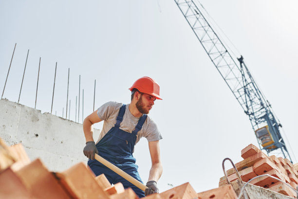 使用showel。身穿制服的年轻建筑工人正在这座未完工的建筑上忙碌图片下载