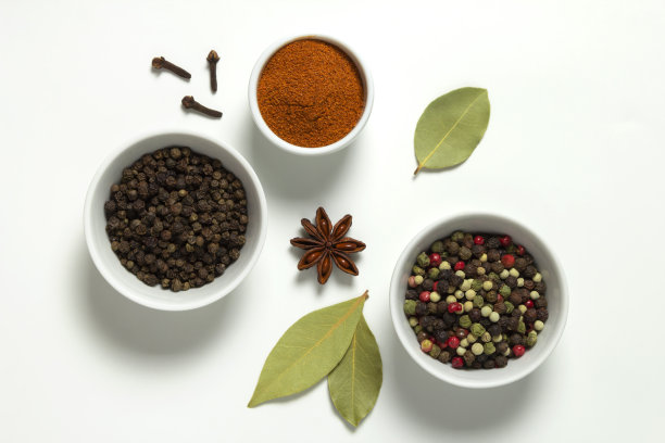 在碗中放入各色花椒和辣椒粉，白色背景上放入月桂叶，茴芹和丁香。图片下载