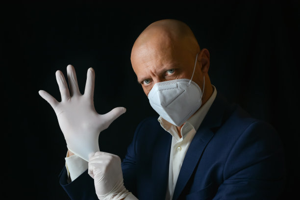 一位优雅的男士戴着医用口罩，把橡胶手套戴在手上。图片下载