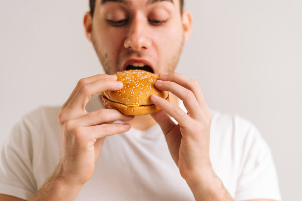近距离的英俊的年轻男子咬吃美味的汉堡在白色孤立的背景。图片下载