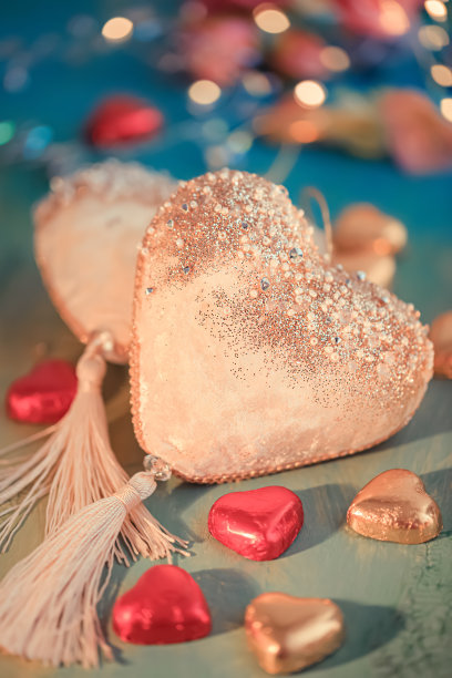 两个天鹅绒心形，金色和红色的箔糖放在一张旧的绿色桌子上。模糊彩色背景与黄色散景图片下载